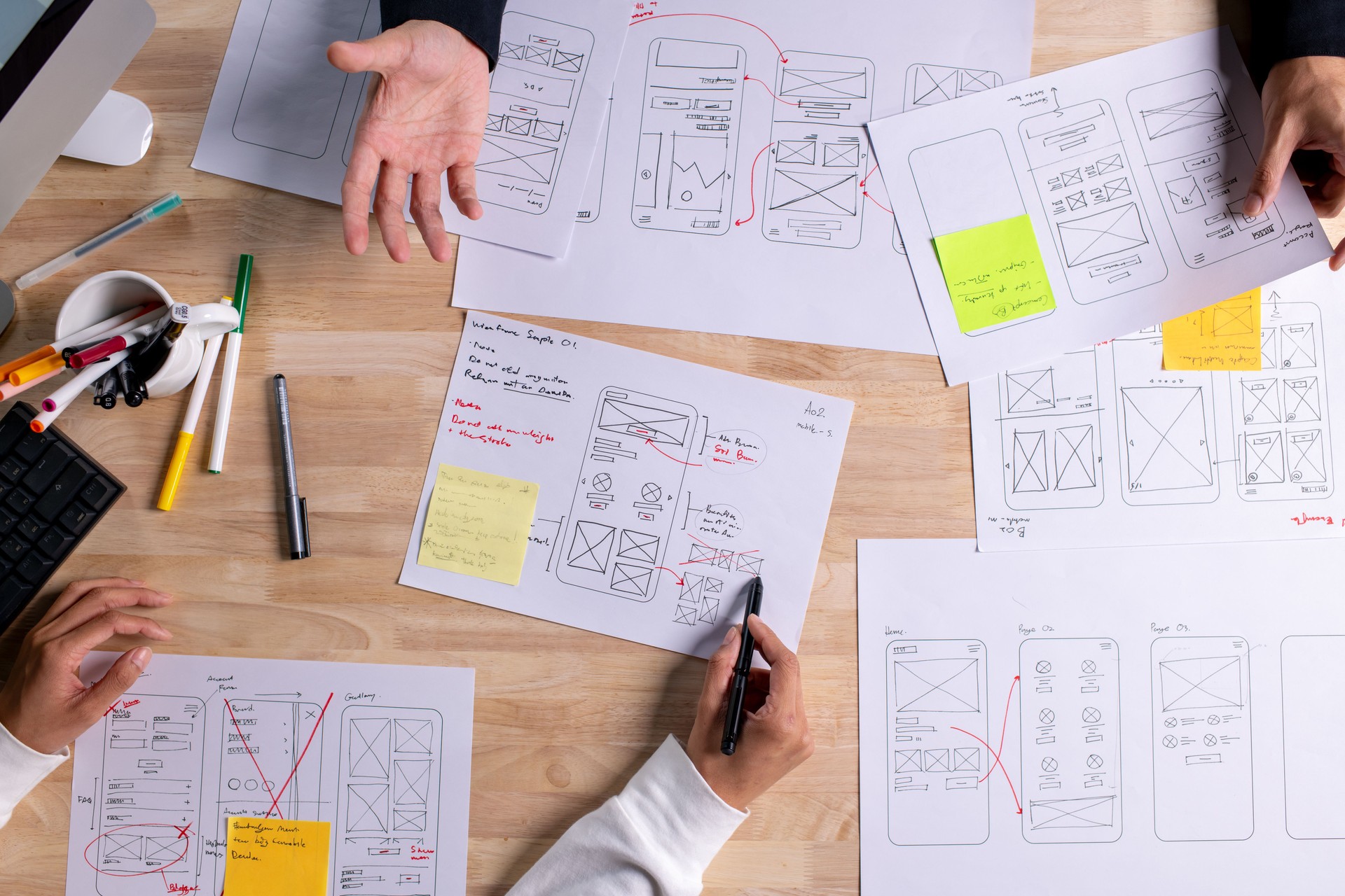 UX UI designers discussing and brainstorming on wireframes for a website and mobile app prototype, surrounded by sketches of user flow and design tools, in the concept of website and mobile application design concept.